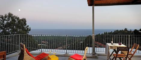 A balcony with wicker furniture, a table with a bottle, and a view of the sea.