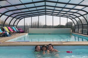 Une piscine dotée d’un toit en verre, entourée de chaises longues.