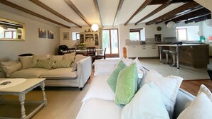 A living room with a sofa, a dining table, and a kitchen area in the background. - Large 3 bedroom gite with heated covered pool & large garden (Henansal)