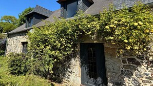 A stone house with a steeply pitched roof, a chimney, and a window with a grid pattern. - Large 3 bedroom gite with heated covered pool & large garden (Henansal)