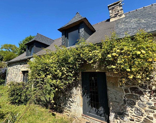Une maison en pierre avec un toit à forte pente, une cheminée et une fenêtre à carreaux.