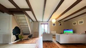 A spacious living area with a wooden floor, a white sofa, a television, and a staircase leading to another room. - Large 3 bedroom gite with heated covered pool & large garden (Henansal)