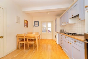 A compact kitchen with wooden flooring, a dining table with chairs, and light-colored cabinets.