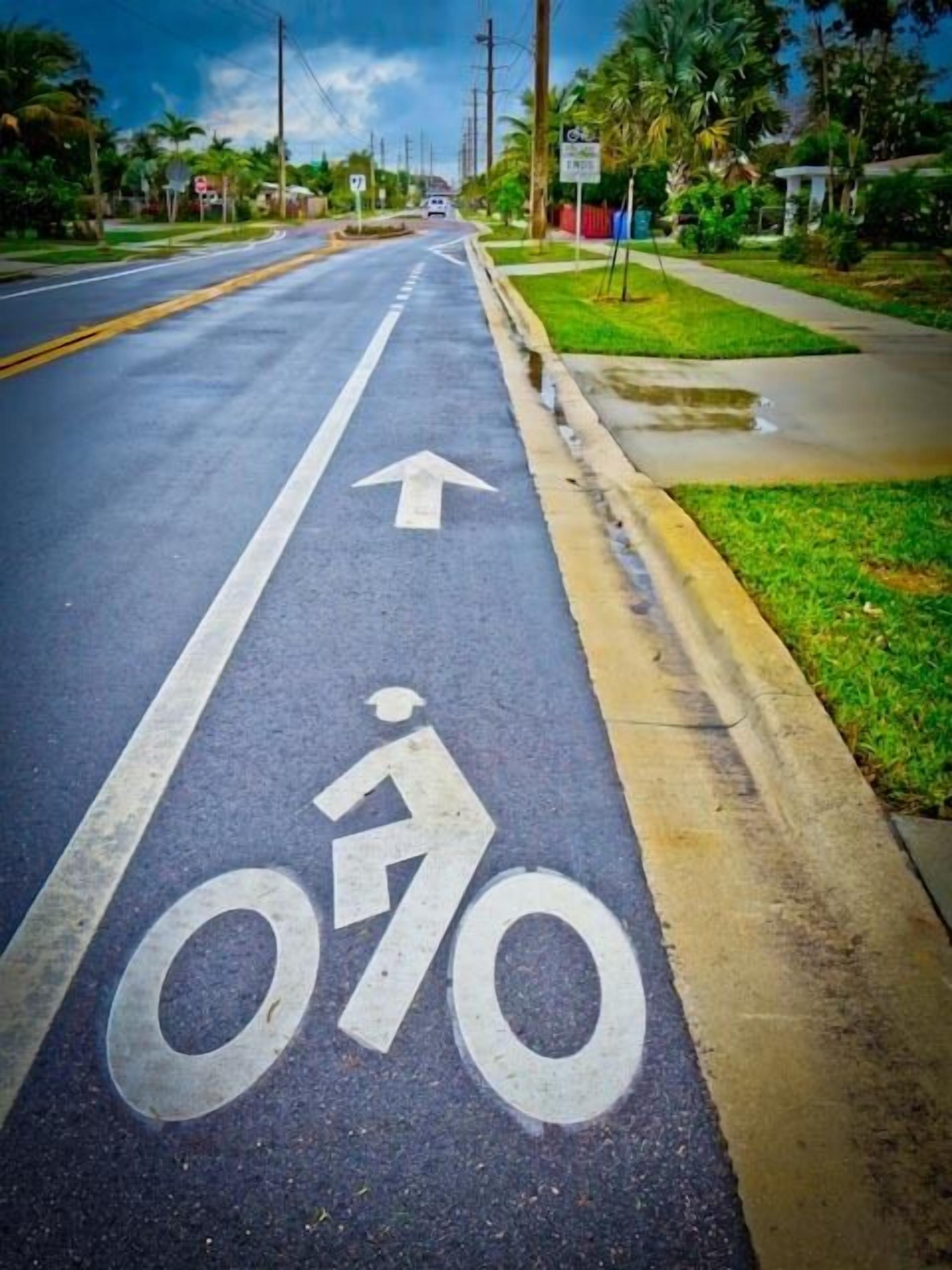 Una calle con carril bici señalizado por un símbolo de bicicleta blanca y una flecha que indica la dirección.