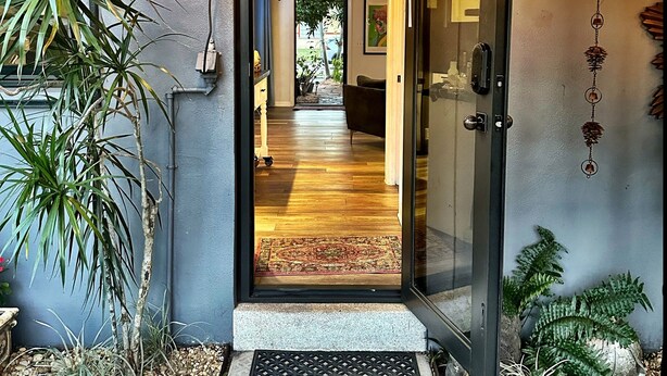 Una entrada moderna con puerta de vidrio, suelo de madera y un pequeño jardín con plantas.