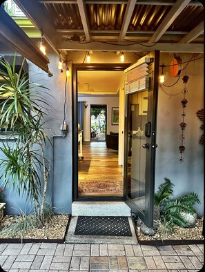 Une entrée moderne avec une porte en verre, un plancher en bois et un petit espace jardin agrémenté de plantes.