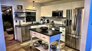 Una cocina moderna con armarios blancos, electrodomésticos de acero inoxidable, una isla central y suelo de madera.
