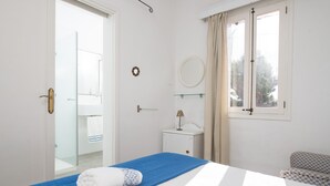A bedroom with a bed, a bedside table, a mirror, and a window with curtains.