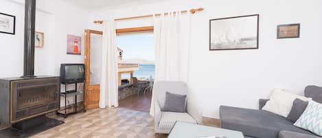Sala de estar com lareira, sofá, poltrona, mesa e vista para o mar por uma porta.