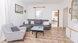 A living room with a checkered armchair, a grey sofa, a glass coffee table, and a white cabinet.