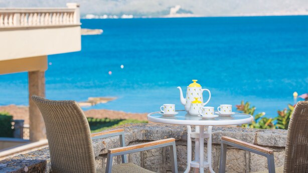A table with a teapot and cups set on a balcony overlooking a body of water.