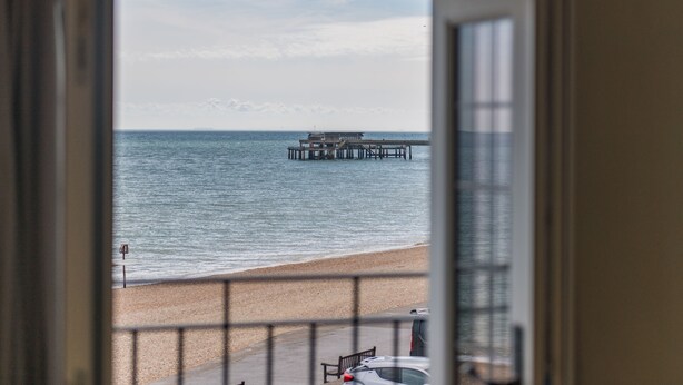 A view of a beach with a pier extending into the water, a sandy shore, and a railing.
