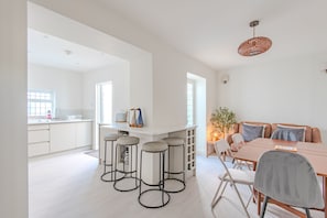A modern kitchen with bar stools, a dining area with a table and chairs, and a hanging light fixture.