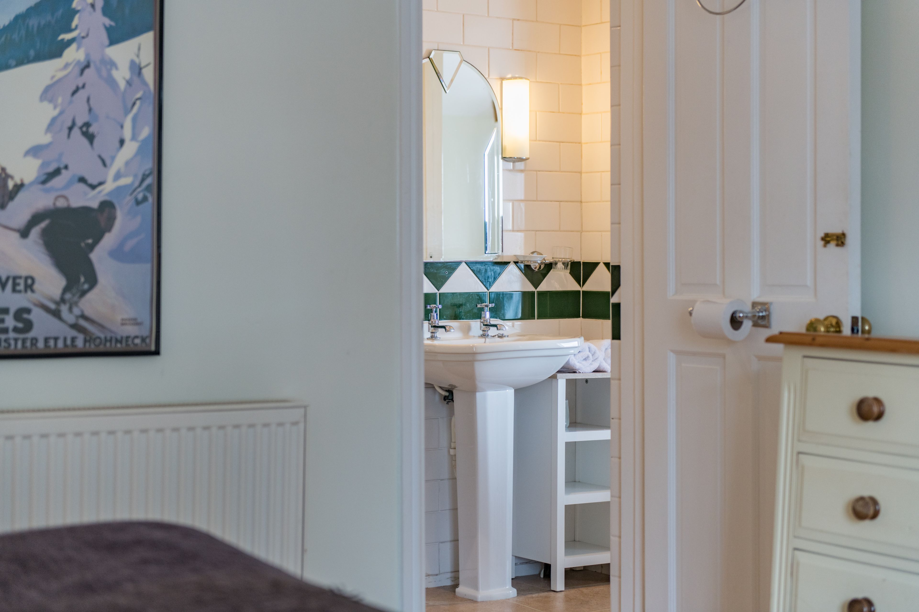 Baño con lavamanos blanco, espejo y un salpicadero de azulejos blancos y verdes.