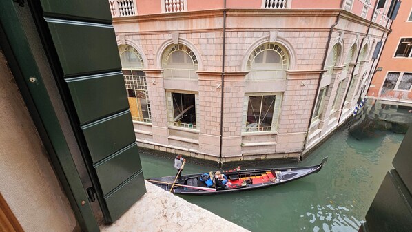 A gondola on a canal with a building featuring arched windows and a balcony.