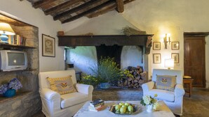 A cozy living room with two white armchairs, a coffee table with a fruit bowl, and a stone fireplace.
