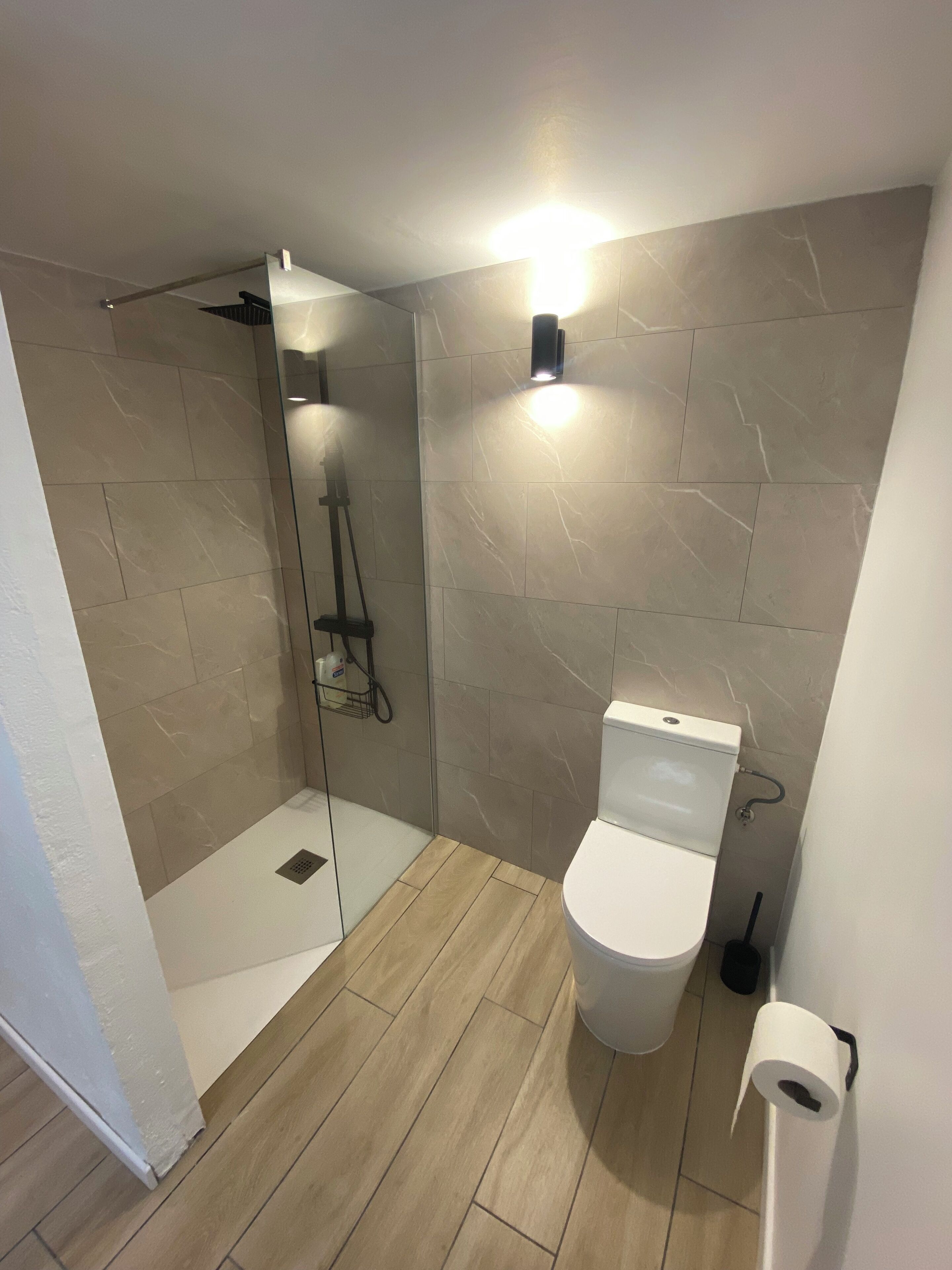 A bathroom with a shower, toilet, and a wall-mounted light fixture.