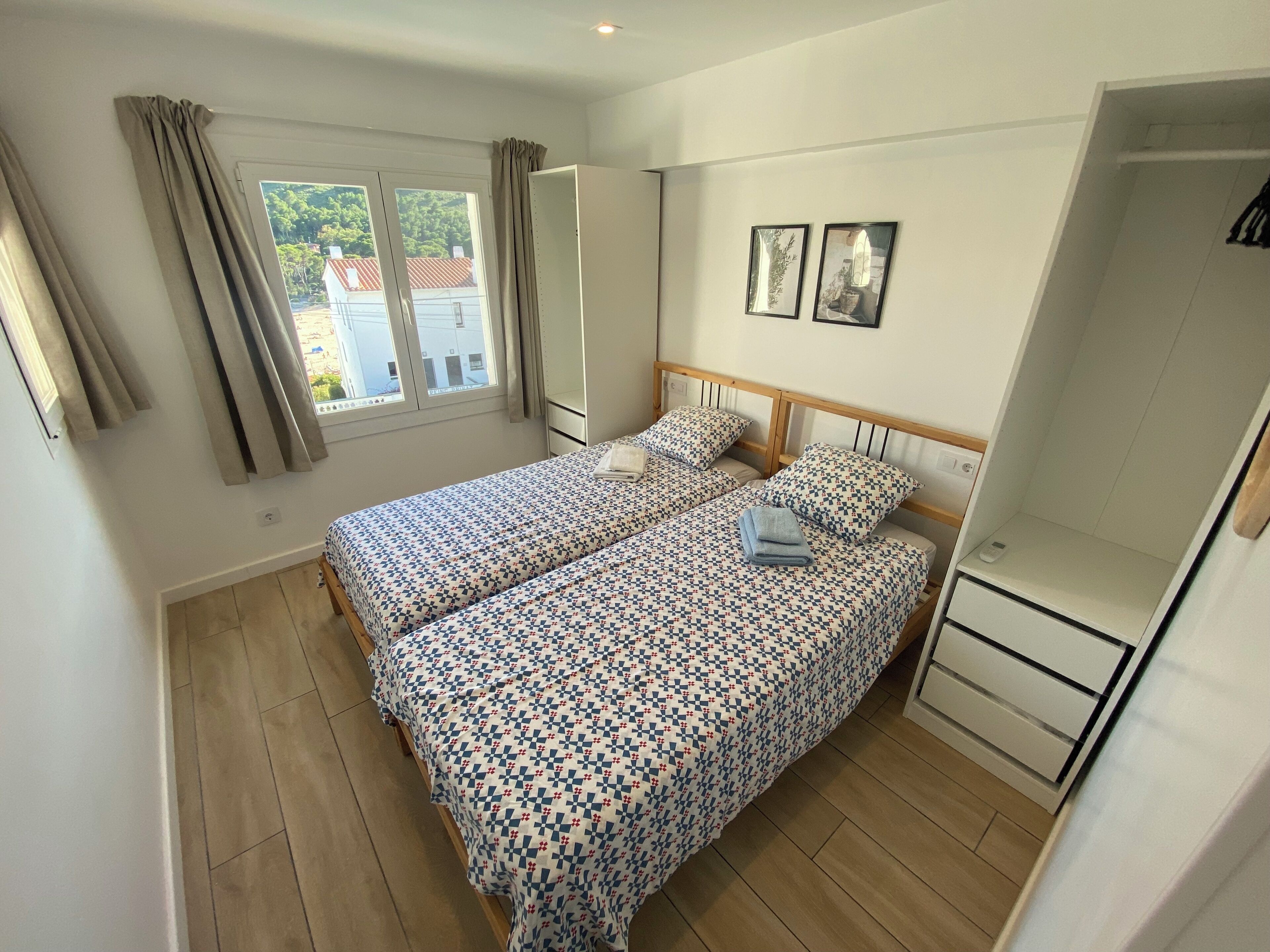 A bedroom with two beds, a window with curtains, a wardrobe, and a small table.