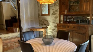 Un coin repas avec une table ronde recouverte d’une nappe à motifs, entourée de chaises noires. Une suspension orange tressée est suspendue au-dessus de la table.