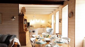 A cozy dining area with a wooden table set for four, a kitchen in the background, and a large window on the right. - In the heart of "Cancale"  garden , 500m sea / garage (Cancale)