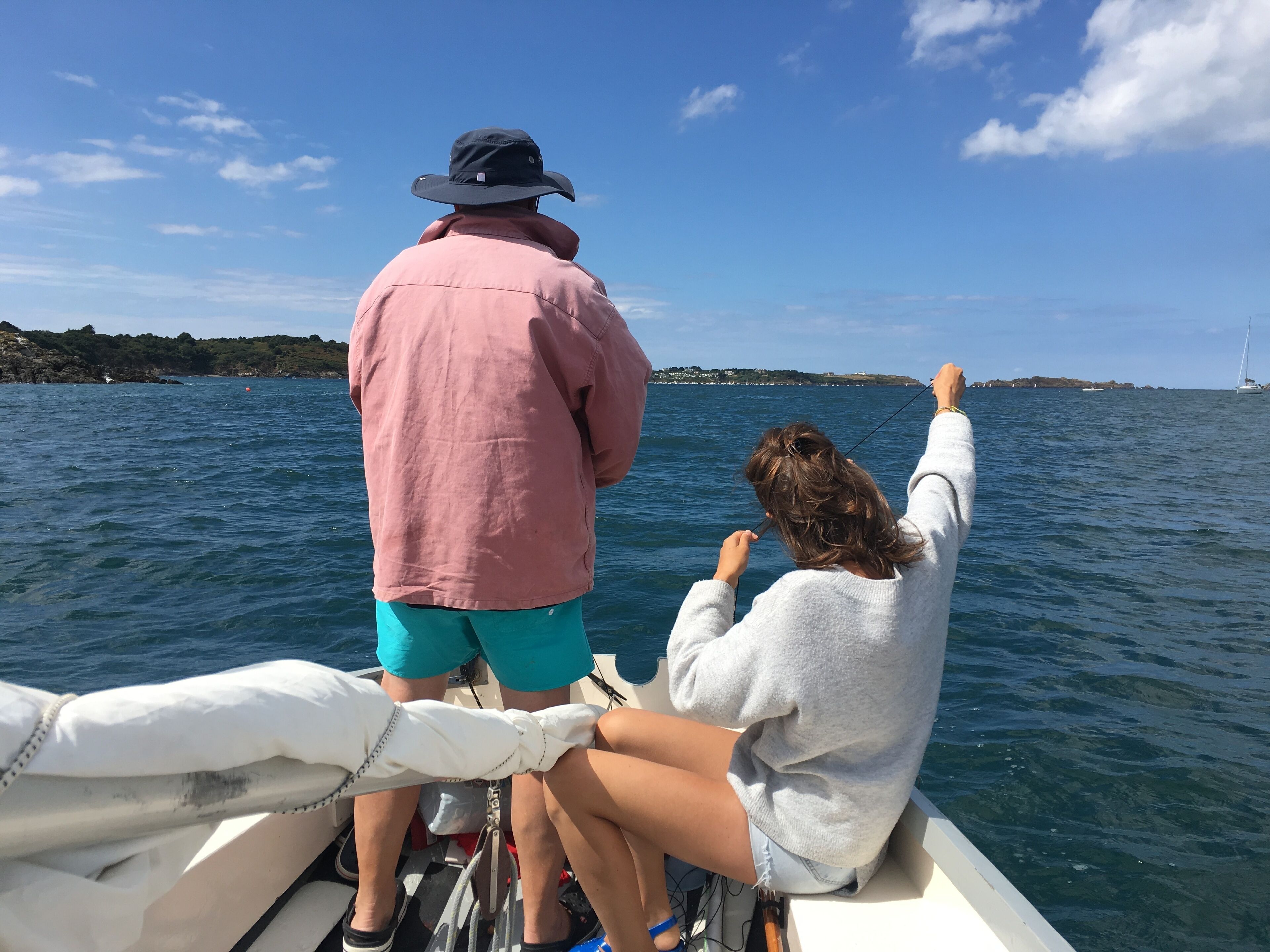 Two people on a boat with a view of the sea and distant land.