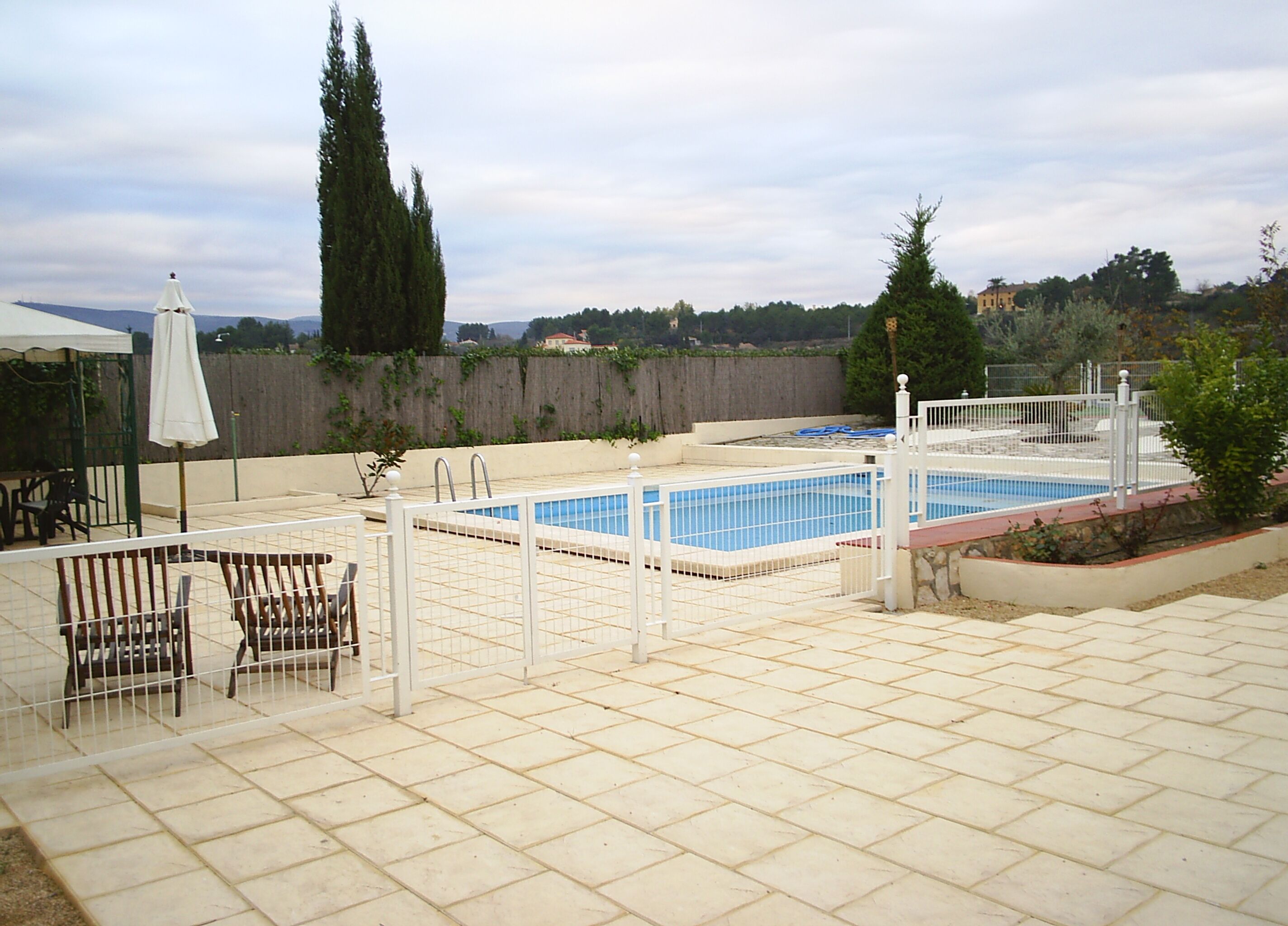 Una piscina rectangular con valla blanca, rodeada de un patio con baldosas.