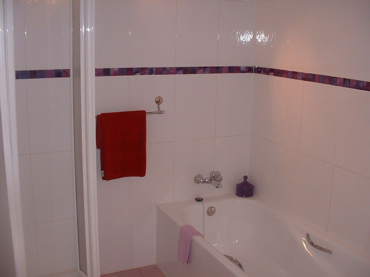 Une salle de bain avec une baignoire, une serviette rouge et une bouteille violette.