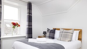 A neatly made bed with a grey blanket, a wooden headboard, and a bedside table with a lamp.