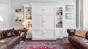 A living room with a large white cabinet, two brown leather sofas, a patterned rug, and framed pictures on the walls.