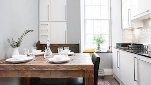 A dining table set with plates, glasses, and cutlery, a wooden chair, a white cabinet, and a window with natural light.