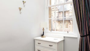 A white bedside table with a lamp and two wall-mounted hooks.