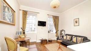 A room with a sofa, a TV, a wooden chair, a table, and a rug.