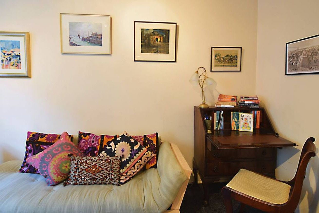A room with a bed, a chair, a desk with books, and framed pictures on the wall.