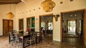 A spacious dining area with a wooden table and chairs, a woven ceiling light, and a view of the outdoor garden through an open doorway. - Beautiful Staffed 5 Bedroom Villa, Very Personal Touch Overlooking Paddy Fields (Pitiduwa in Talpe Pattuwa)