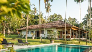 A poolside view of a resort with a white building, palm trees, and lounge chairs. - Beautiful Staffed 5 Bedroom Villa, Very Personal Touch Overlooking Paddy Fields (Pitiduwa in Talpe Pattuwa)