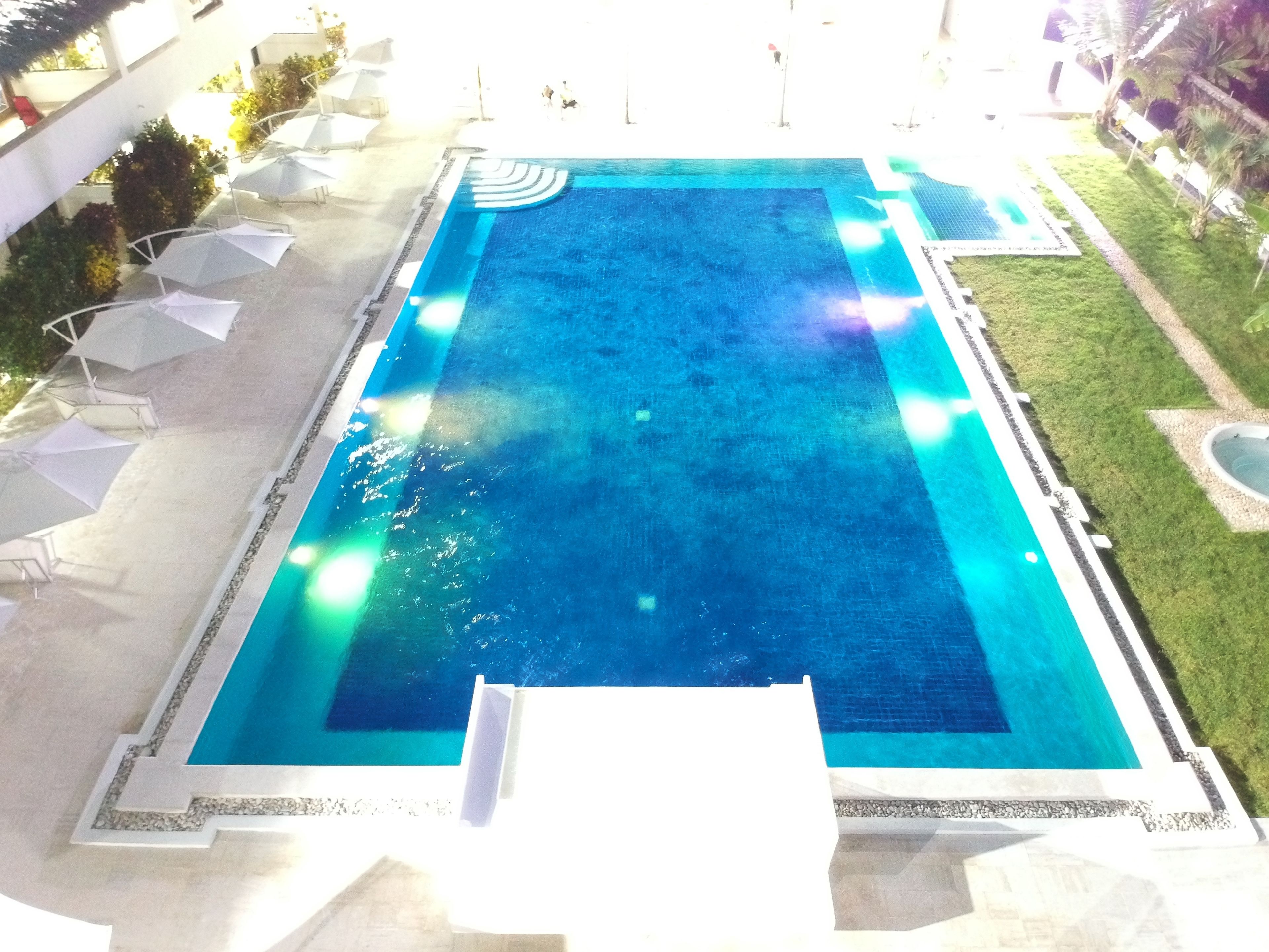 A rectangular swimming pool with a tiled edge, surrounded by a grassy area and white umbrellas.
