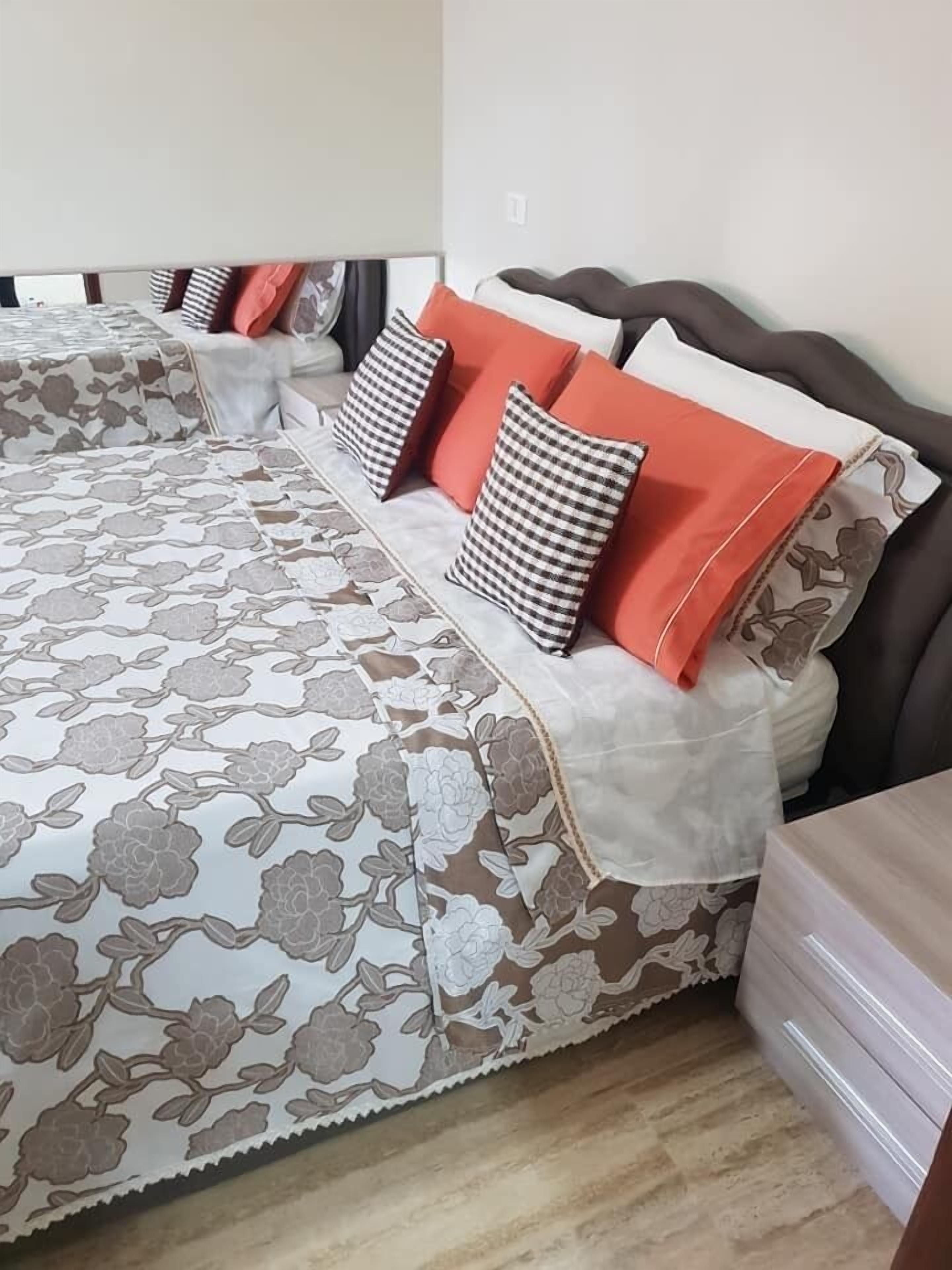 A neatly made bed with floral-patterned bedding and multiple pillows in various colors.