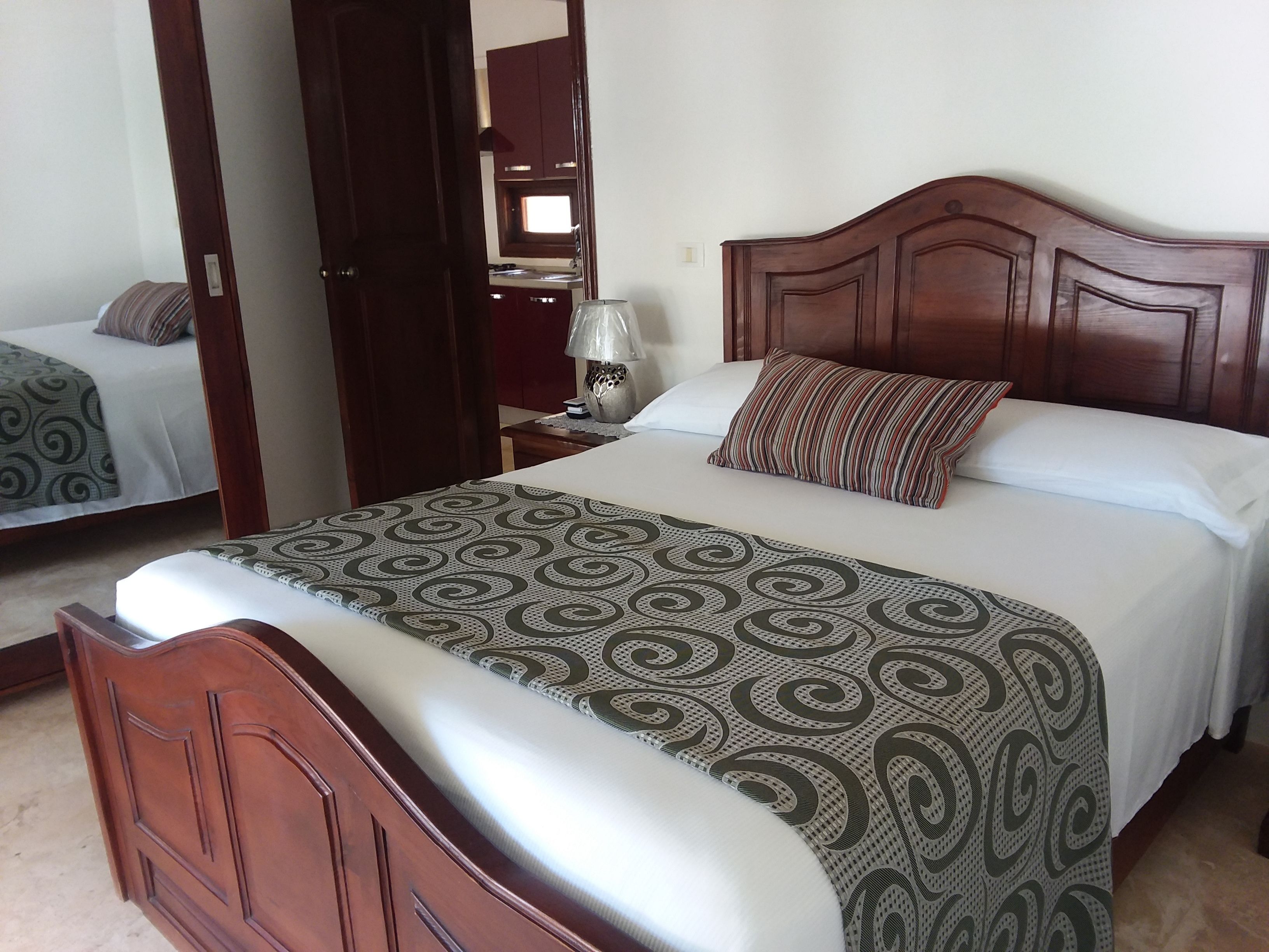 Una habitación de hotel con una cama grande, un cabecero de madera, una mesita de noche con lámpara y un espejo en la pared.