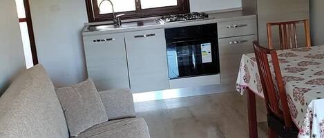 A modern kitchen with a gas stove, oven, and dishwasher, a dining area with a table and chairs, and a sofa in a living area.