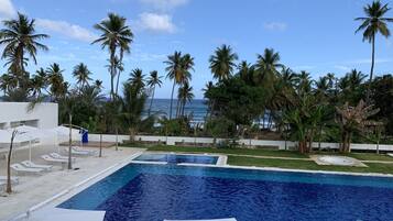 Uma piscina com água azul cristalina, rodeada por palmeiras e vista para o oceano.