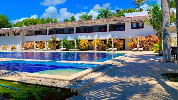 Un hôtel doté d’une piscine, de chaises longues et d’un bâtiment au toit de chaume.