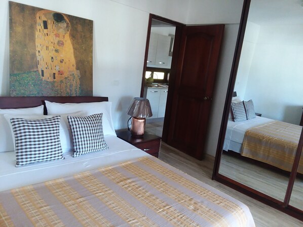 A hotel room with a large bed, a bedside table with a lamp, a mirror, and a painting on the wall.