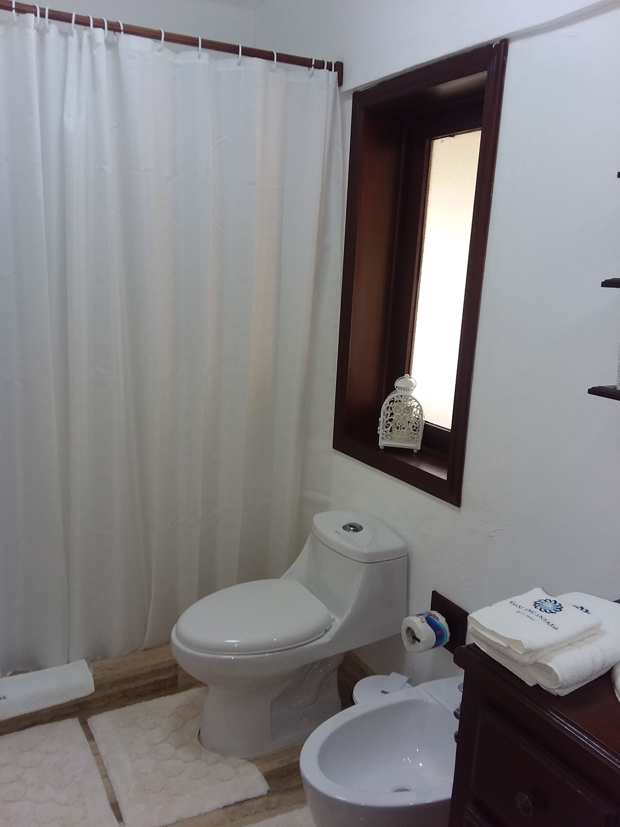 A bathroom with a toilet, bidet, and a small window with a decorative item.