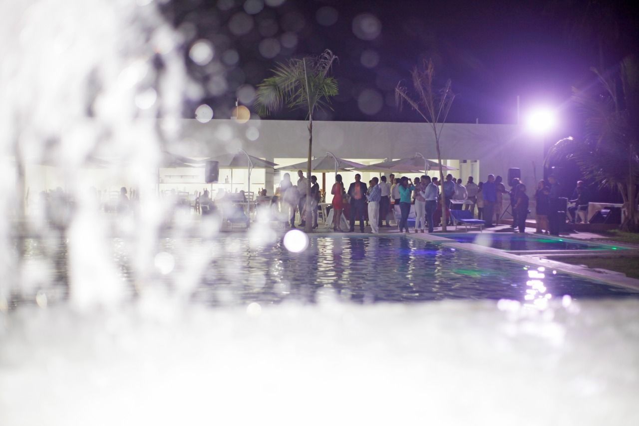 A nighttime outdoor gathering with a fountain, palm trees, and a building in the background.