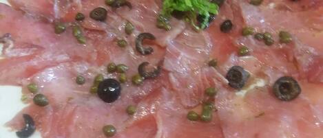 A plate of thinly sliced cured meat garnished with capers and olives.