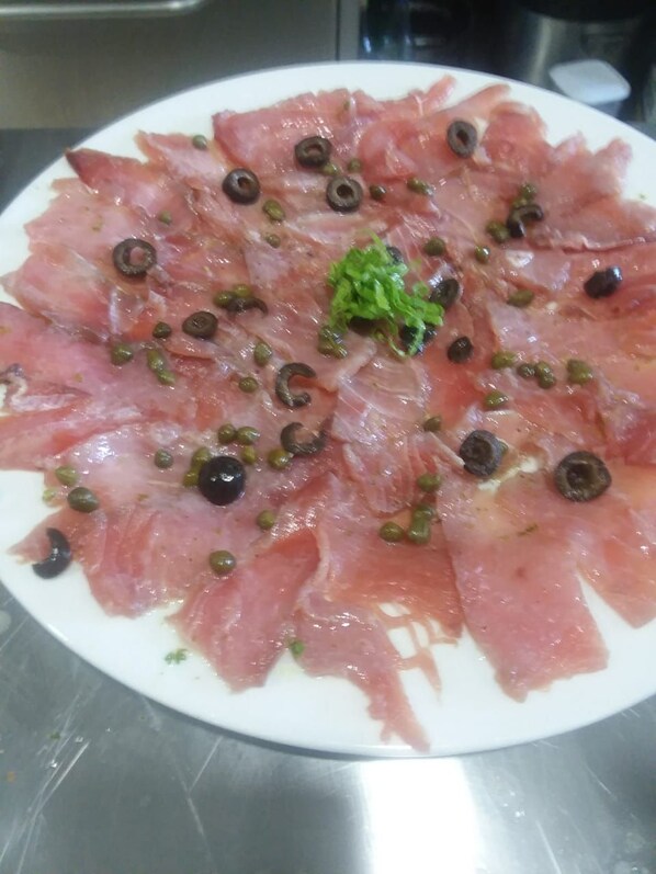 Un plato de carne curada en lonchas finas, decorado con alcaparras y aceitunas.