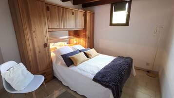 Een slaapkamer met een houten garderobe, een bed met een wit- en blauwe dekbedovertrek, een stoel en een klein raam.