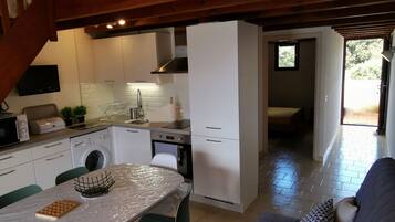 Een moderne keuken met een ingebouwde oven, magnetron en wasmachine. Er is een eethoek met een tafel en stoelen, en een bank in de woonkamer.