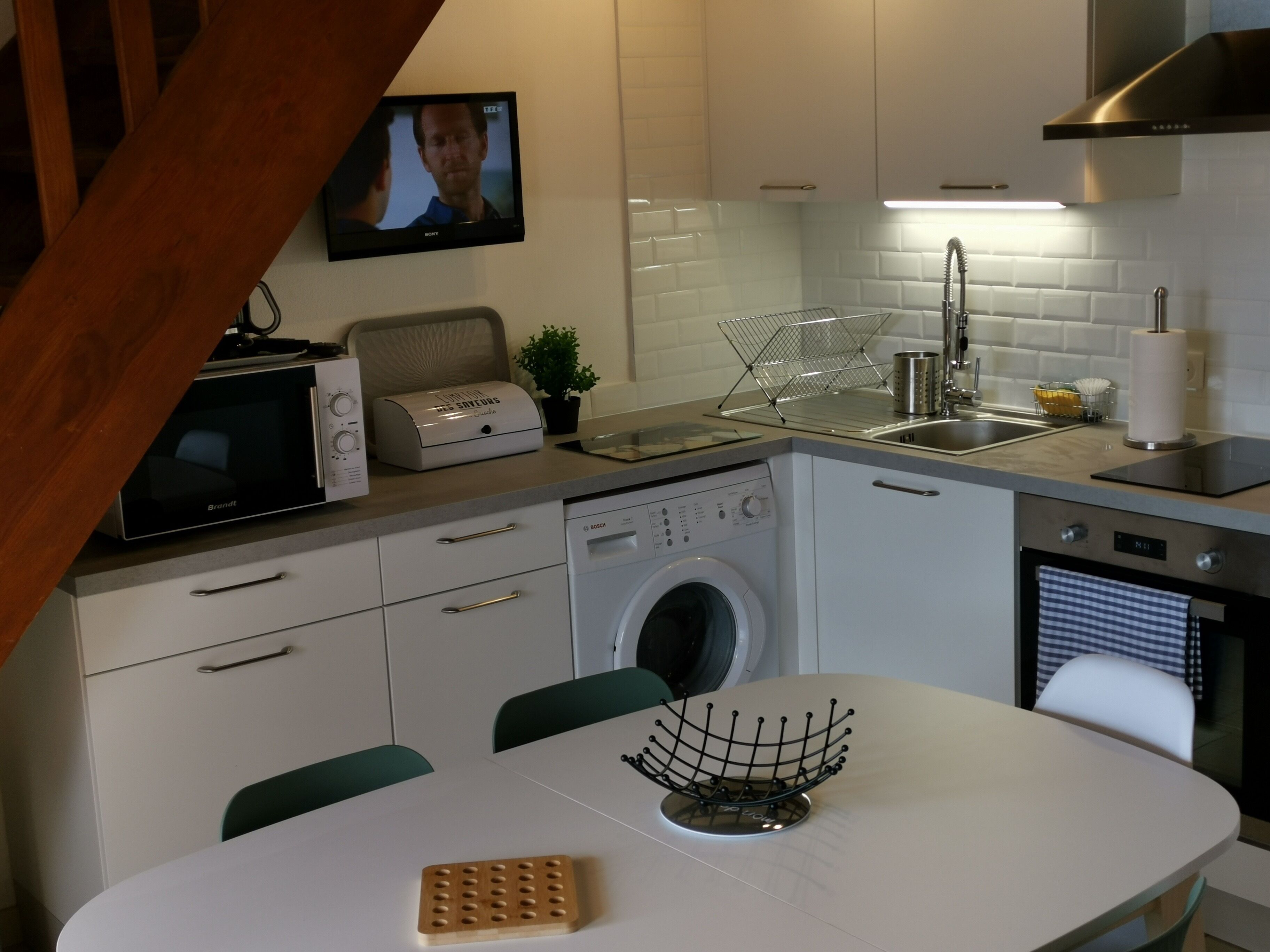A modern kitchen with white cabinets, a Bosch washing machine, a microwave, and a sink.