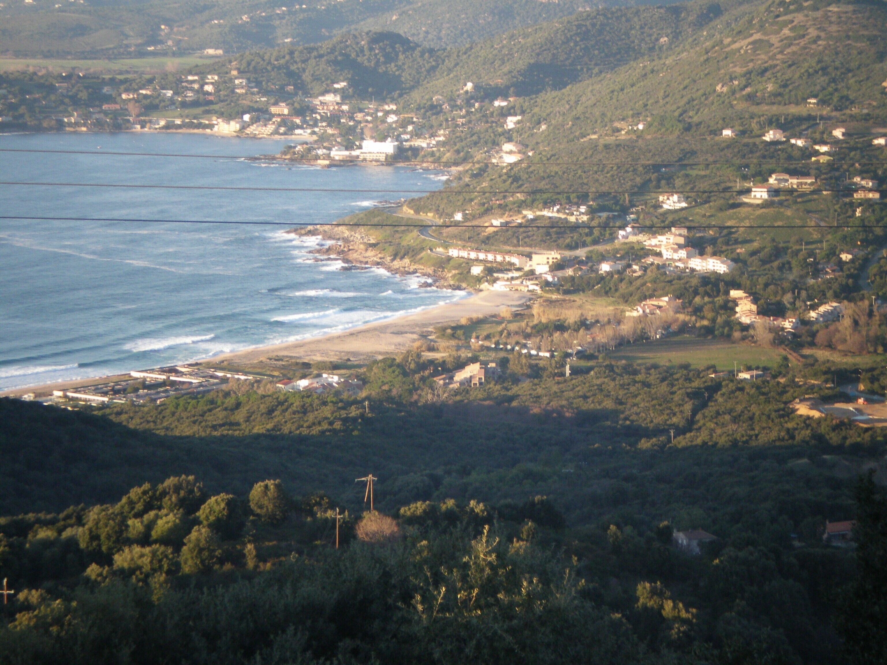 Un paysage côtier avec une plage, des maisons et de la végétation.
